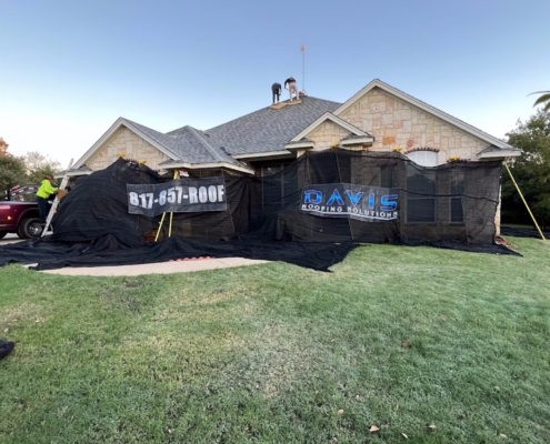 Stone-front home during a roof replacement with crew on the ridge and a worker climbing a ladder.