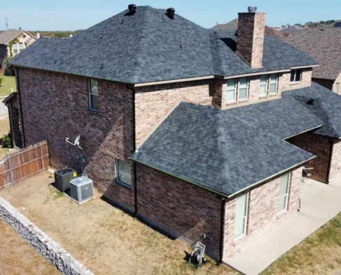 Aerial of a two-story brick home with a new charcoal shingle roof and brick chimney