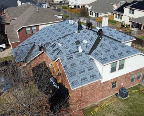 Aerial of a two-story home covered in ABC underlayment with roofers working near the peak