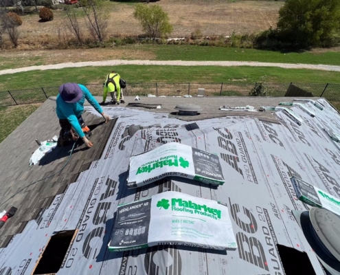Roofers installing synthetic underlayment with Malarkey Highlander shingle bundles staged on the roof