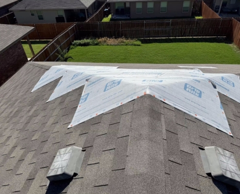 Elevated view of a shingle roof with synthetic underlayment laid in the valley beside box vents.
